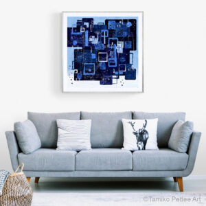 A big paper print of Await My Dreams is in a glass frame. It is on the wall above light blue modern couch.